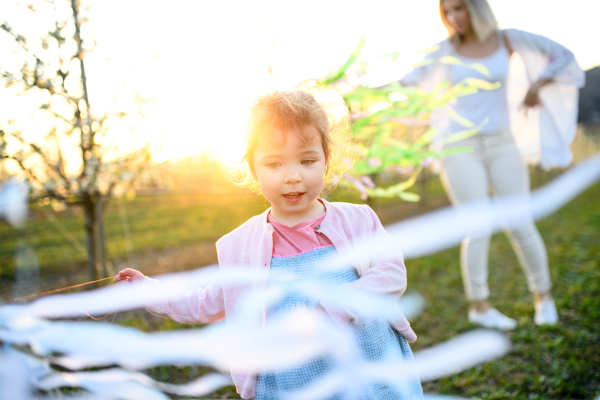 Small girl with unrecognizable mother playing outdoors in spring nature at sunset.