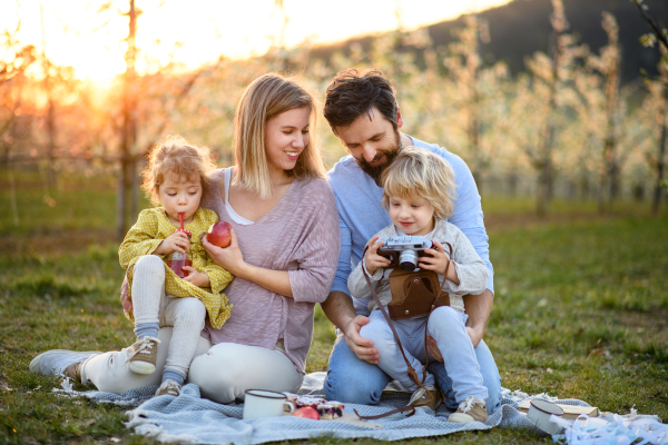 Front view of family with two small children having picnic outdoors in spring nature at sunset.