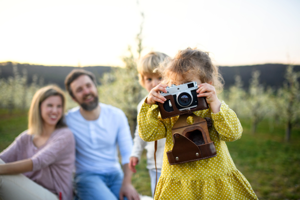 Family with two small children sitting outdoors in spring nature, taking photos.