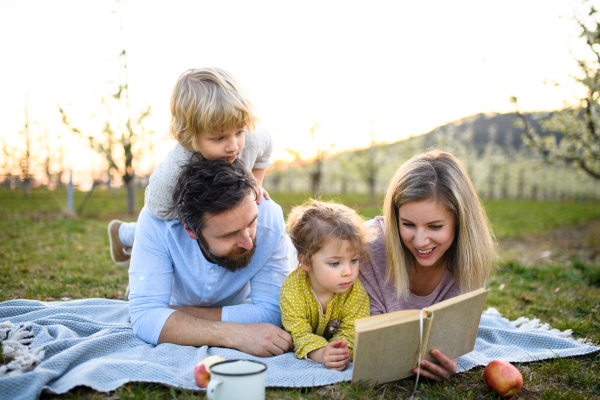 Family and two small children with camera and book outdoors in spring nature resting.