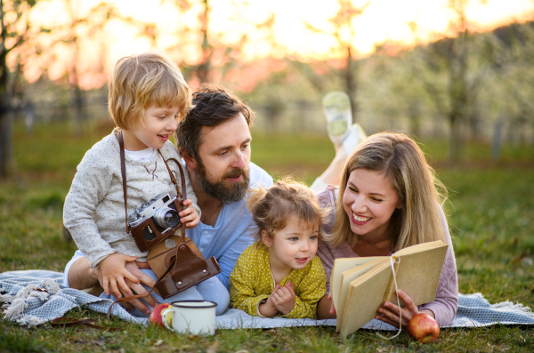 Family and two small children with camera and book outdoors in spring nature resting.