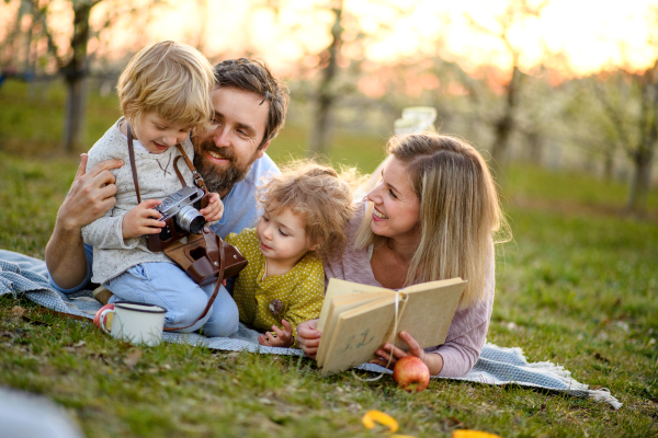 Family and two small children with camera and book outdoors in spring nature resting.