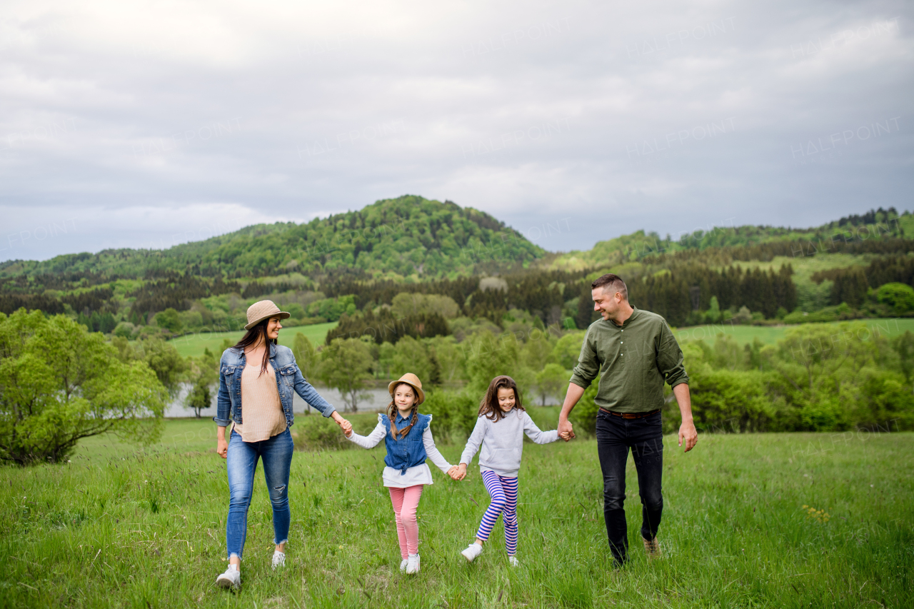 Happy family with two small daughters walking outdoors in spring nature, holding hands.