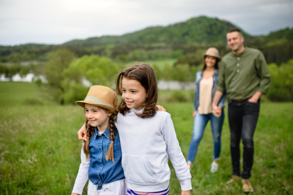 Happy family with two small daughters walking outdoors in spring nature, holding hands.