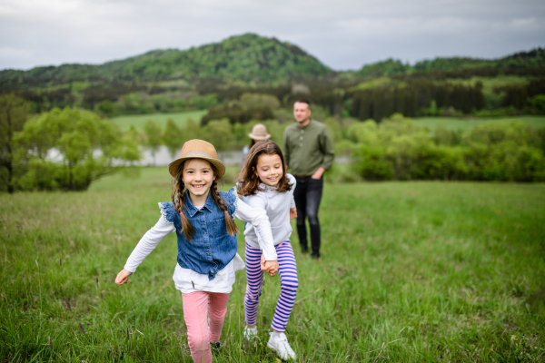 Happy family with two small daughters running outdoors in spring nature, holding hands.