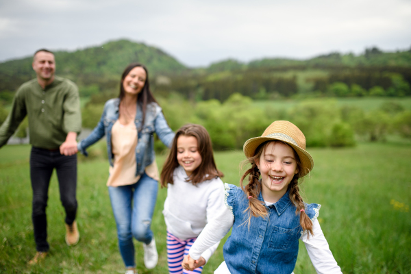 Happy family with two small daughters running outdoors in spring nature, holding hands.