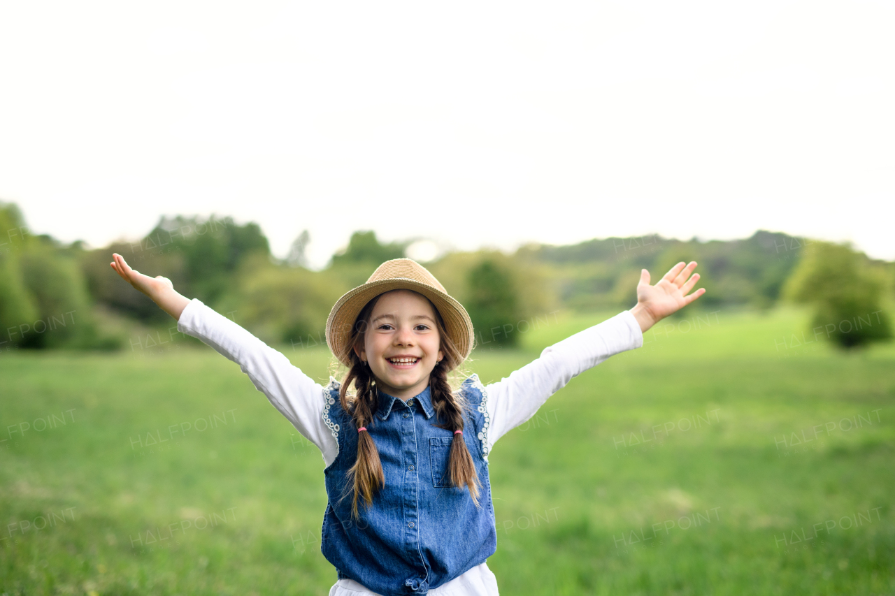 Front view portrait of small girl standing outdoors in spring nature, looking at camera.