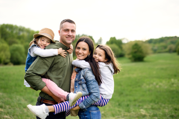 Happy family with two small daughters standing outdoors in spring nature, looking at camera.