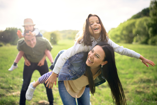 Happy family with two small daughters having fun outdoors in spring nature, giving piggyback ride.