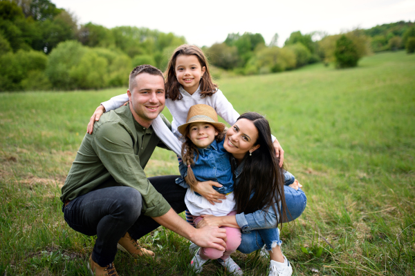 Front view of happy family with two small daughters sitting outdoors in spring nature, looking at camera.