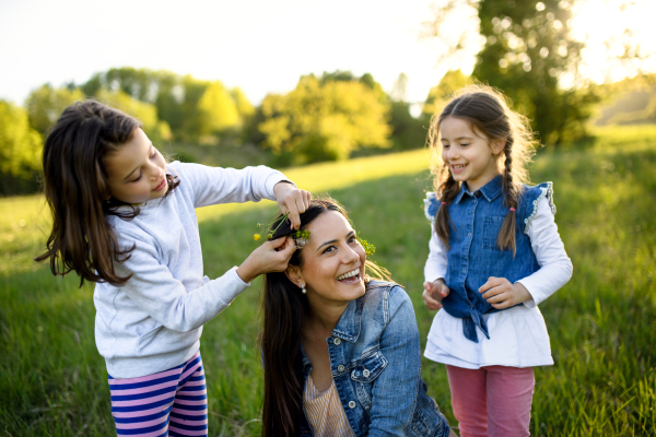 Front view of mother with two small daughters having fun outdoors in spring nature, putting flowers in hair.