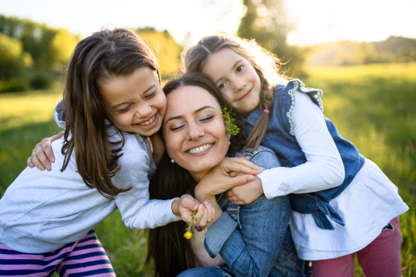 Front view of mother with two small daughters having fun outdoors in spring nature, hugging.