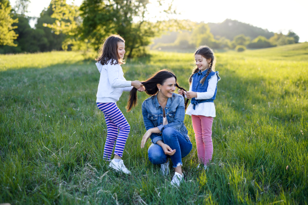 Front view of mother with two small daughters having fun outdoors in spring nature, playing with hair.