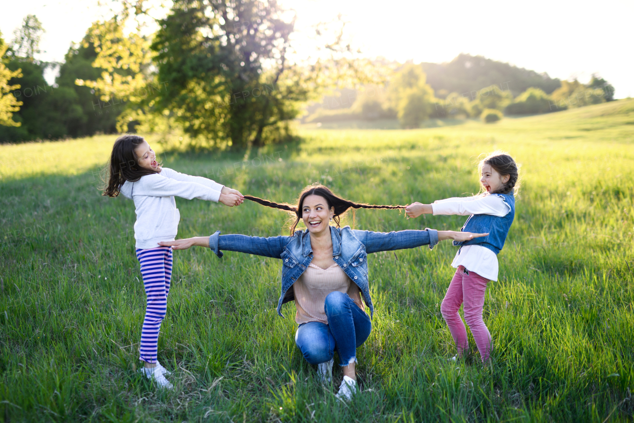 Front view of mother with two small daughters having fun outdoors in spring nature, pulling hair.