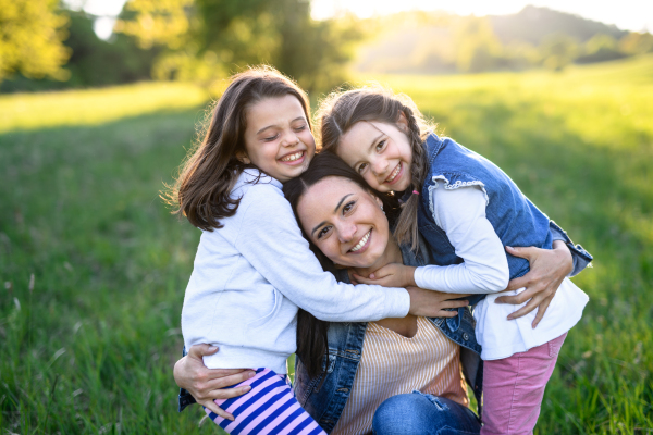 Front view of mother with two small daughters having fun outdoors in spring nature, hugging.