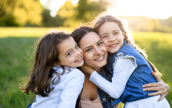 Front view of mother with two small daughters having fun outdoors in spring nature, hugging.