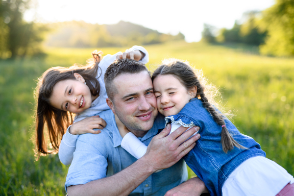 Front view of father with two small daughters having fun outdoors in spring nature, hugging.