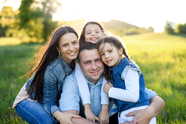 Front view of happy family with two small daughters sitting outdoors in spring nature, looking at camera.