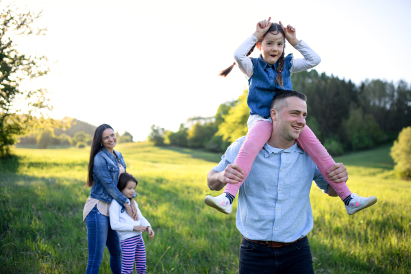 Happy family with two small daughters having fun outdoors in spring nature, giving piggyback ride.