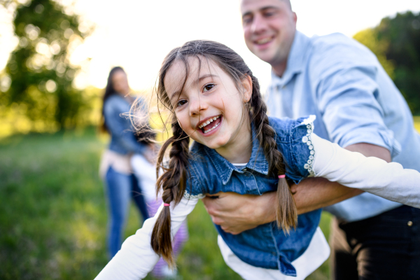 Front view of father playing with small daughter outdoors in spring nature, having fun.