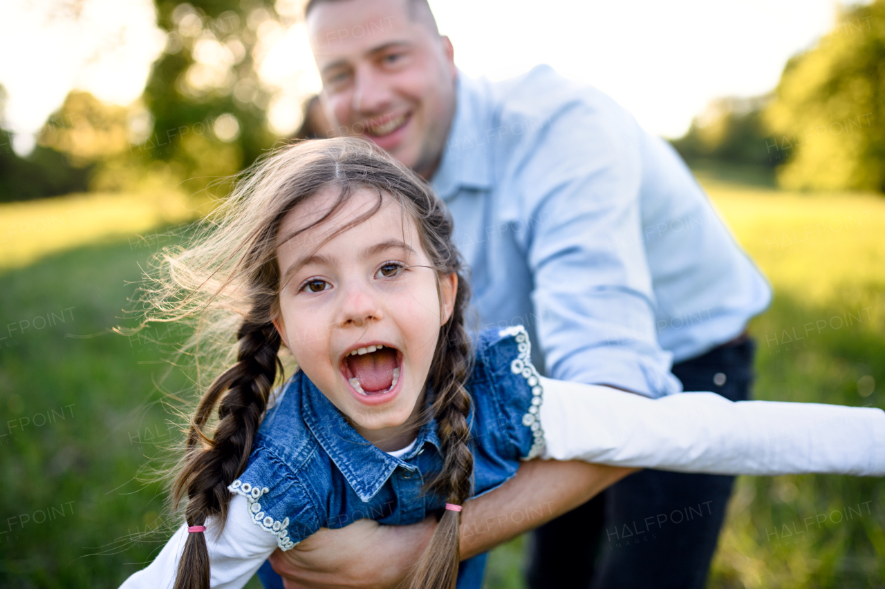 Front view of father playing with small daughter outdoors in spring nature, having fun.