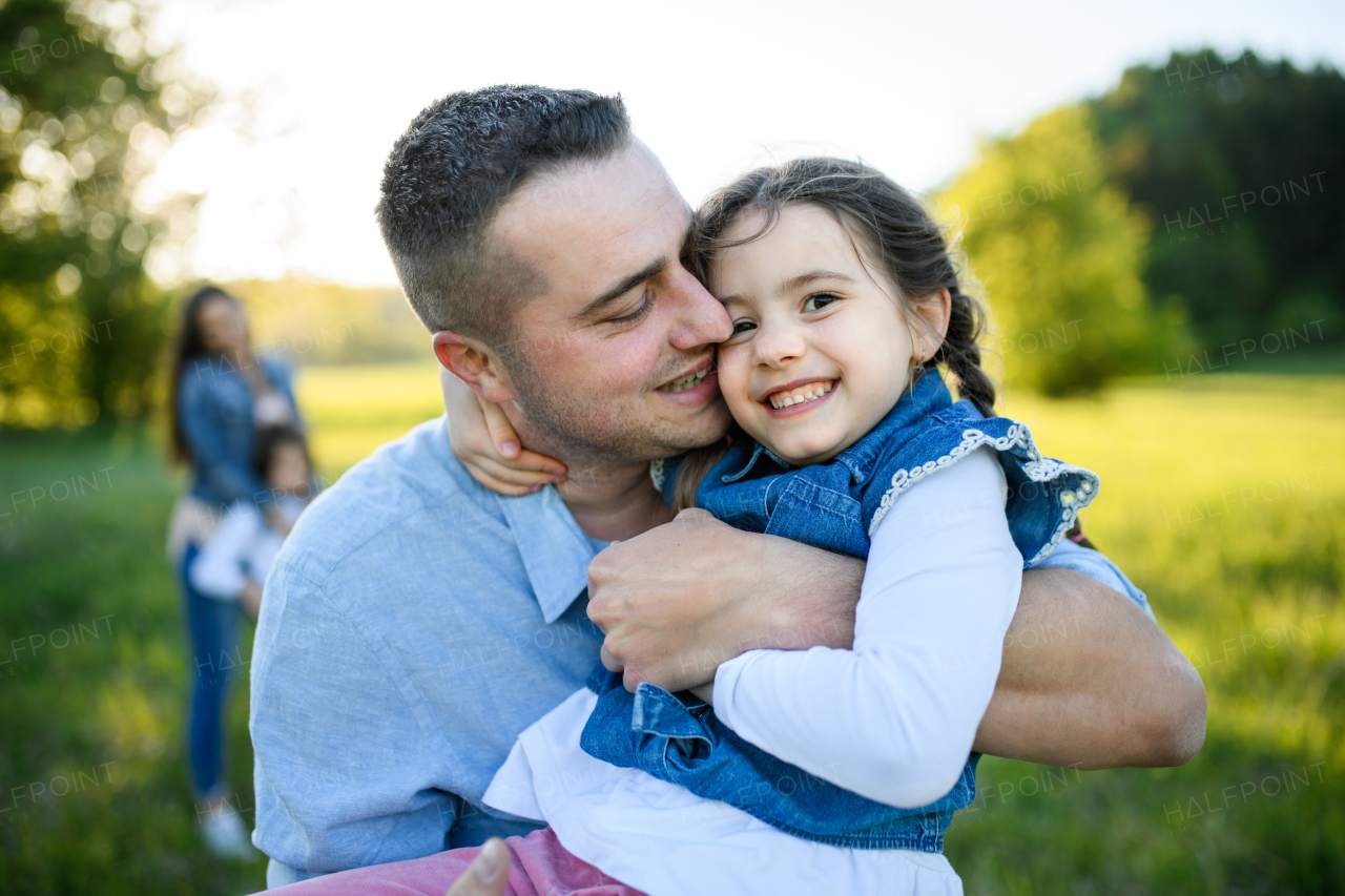 Front view of father playing with small daughter outdoors in spring nature, having fun.