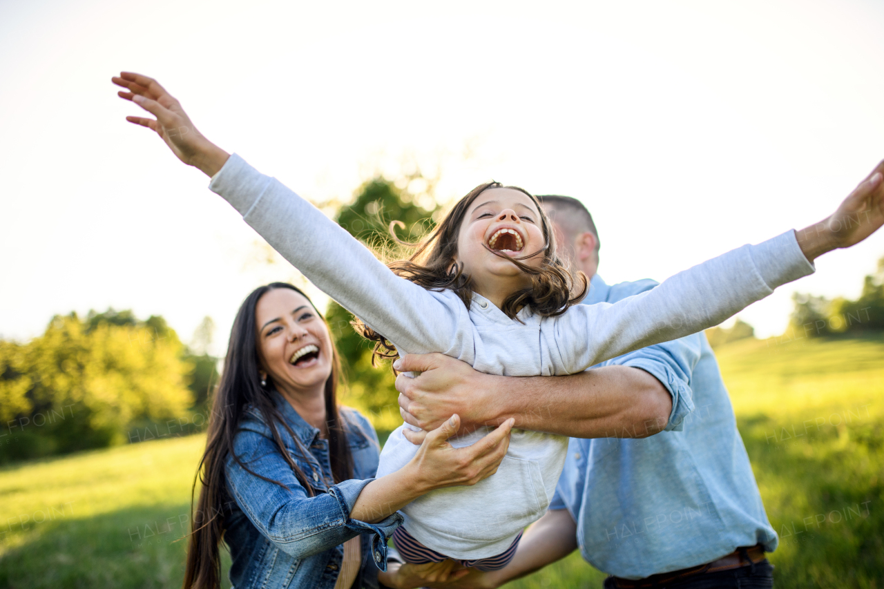 Front view of happy family with small daughter having fun outdoors in spring nature.