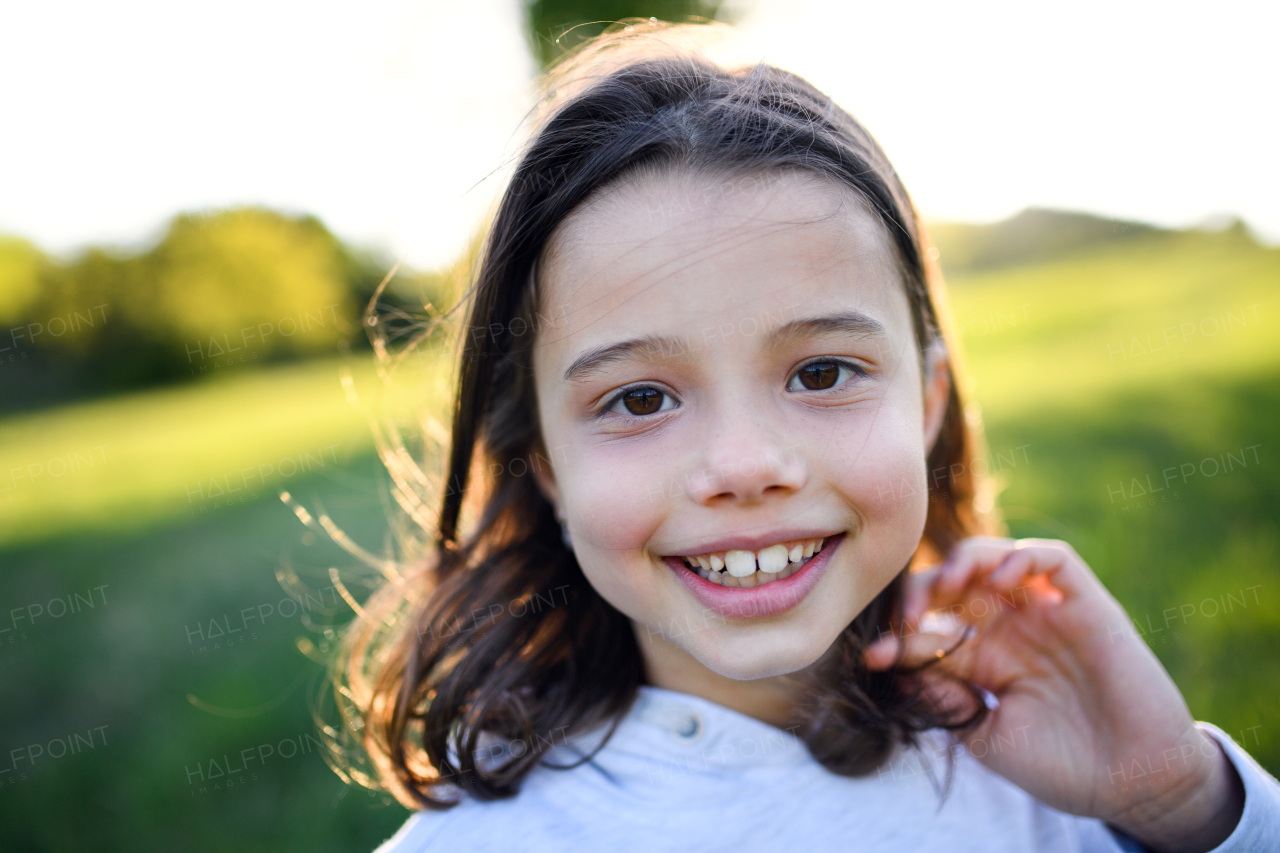 Front view portrait of small girl standing outdoors in spring nature, looking at camera.