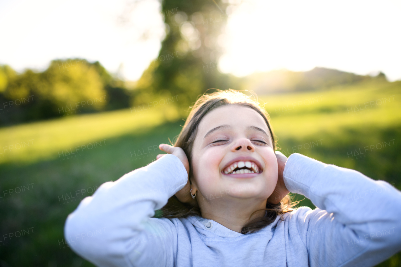 Close-up portrait of small girl standing outdoors in spring nature, having fun.