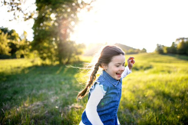 Portrait of cheerful small girl running outdoors in spring nature, laughing.