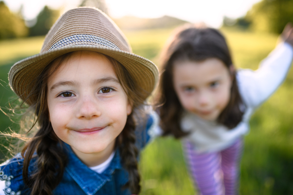 Front view portrait of two small girls standing outdoors in spring nature, looking at camera.