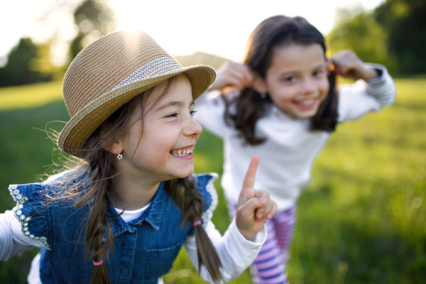 Front view portrait of two small girls standing outdoors in spring nature, laughing.