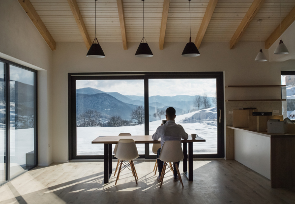 A rear view of mature man sitting at the table in new home, using tablet.