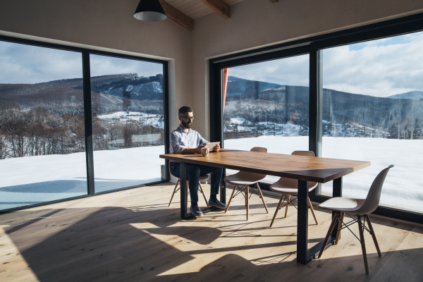 A mature man sitting at the table in new home, using tablet. Copy space.