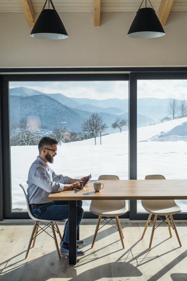 A mature man sitting at the table in new home, using tablet. Copy space.