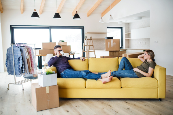 A young couple with cup of coffee sitting on sofa, moving in new home.