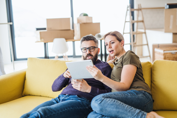 A happy young couple with tablet sitting on sofa, moving in new home.