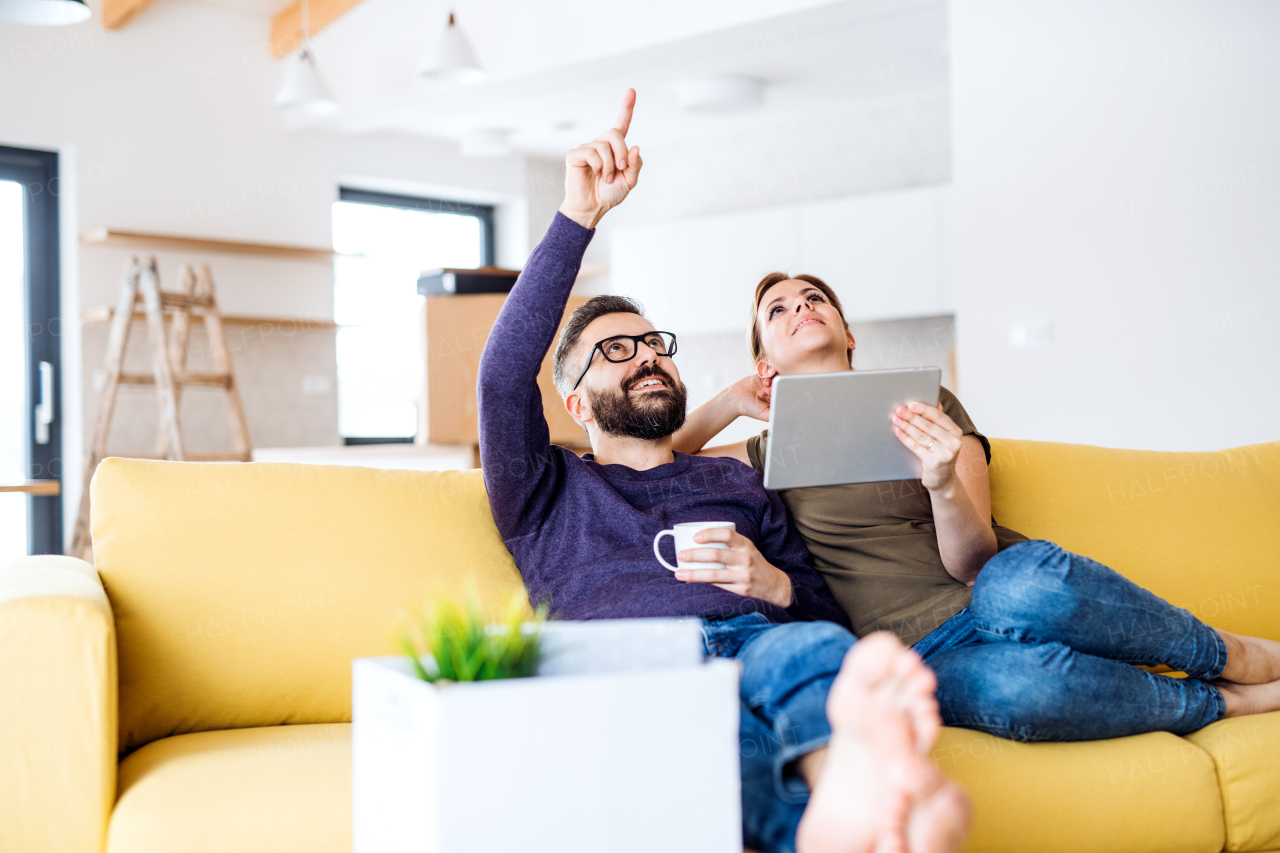 A happy young couple with tablet sitting on sofa, moving in new home.