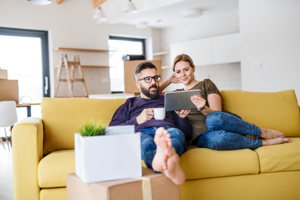 A young couple with tablet and cup of coffee sitting on sofa, moving in new home.