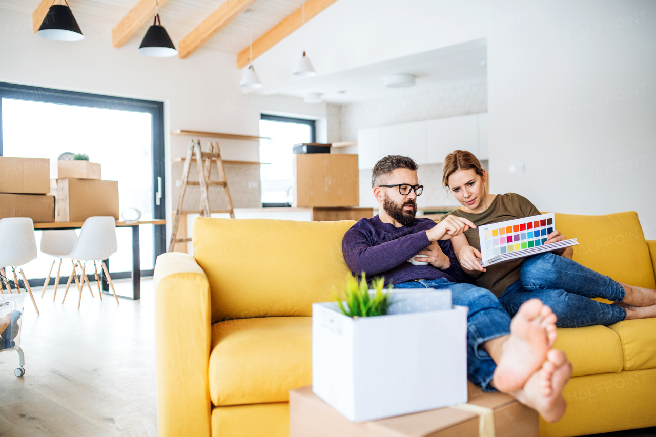 A young couple with color samples sitting on sofa, moving in new home and talking.