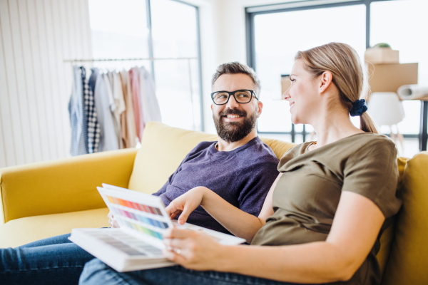 A young couple with color samples sitting on sofa, moving in new home and talking.