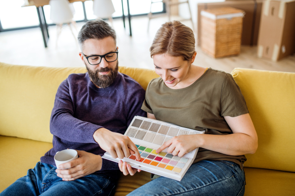 A young couple with color samples sitting on sofa, moving in new home and talking.