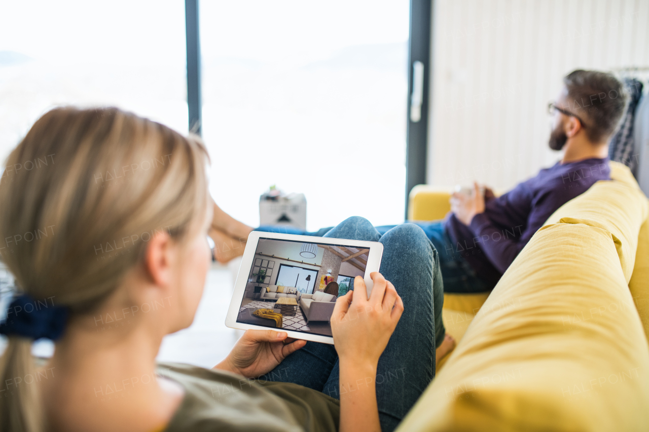 A young couple with tablet sitting on sofa, looking at interior design sketches.