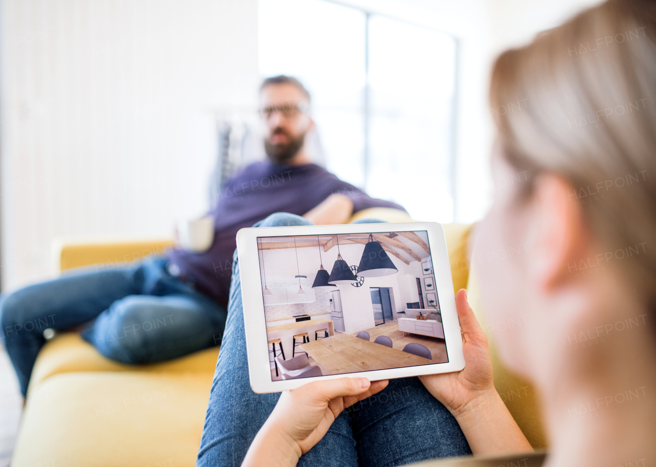 A young couple with tablet sitting on sofa, looking at interior design sketches.