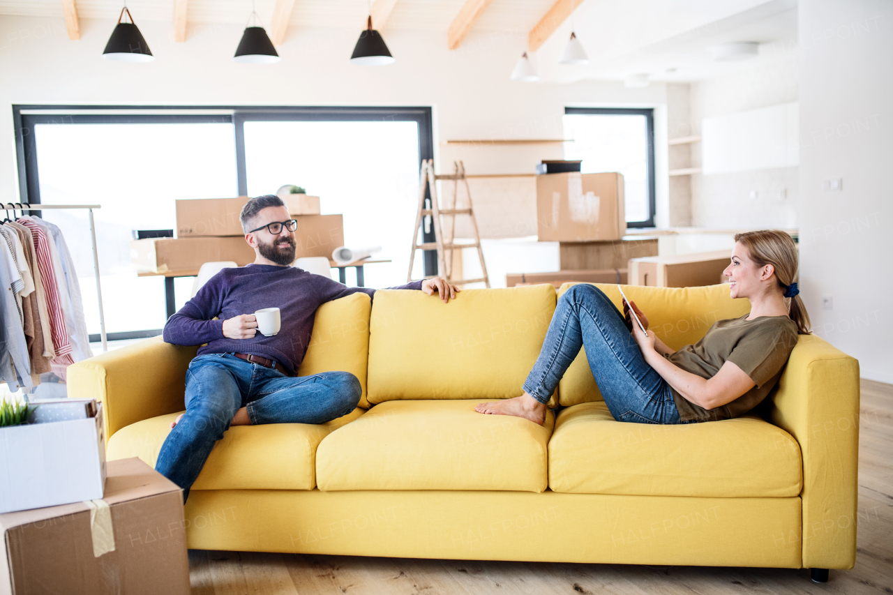 A young couple with tablet and cup of coffee sitting on sofa, moving in new home.