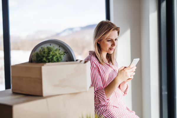 A happy young woman with smartphone moving in new home, text messaging.