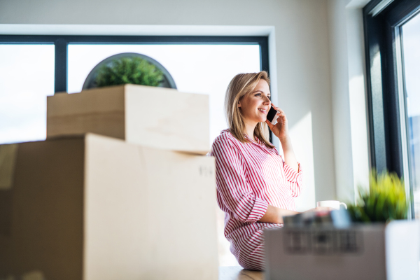 A happy young woman with smartphone moving in new home, making a phone call.