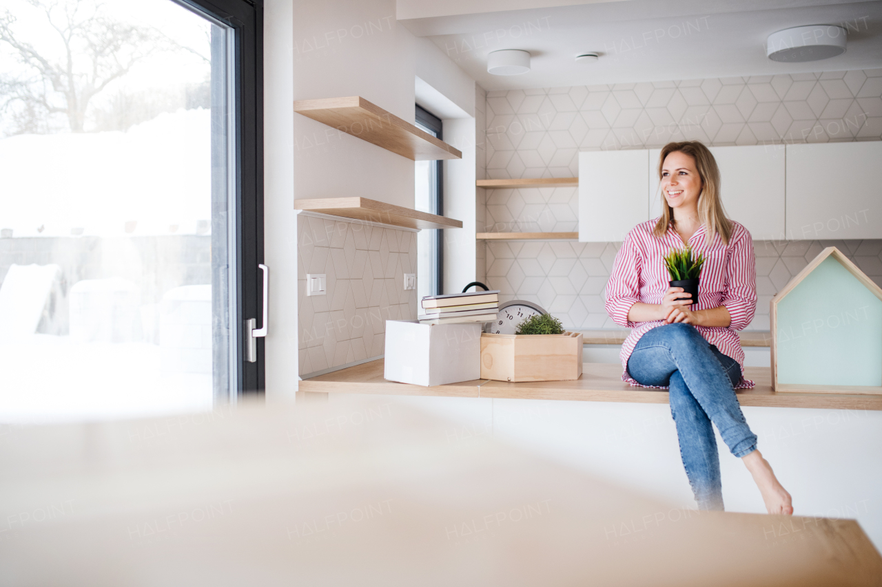 A happy young woman moving in new home, sitting on a counter in the kitchen.