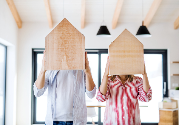 A young couple with wooden houses in front of their head, a moving in new home concept. Copy space.