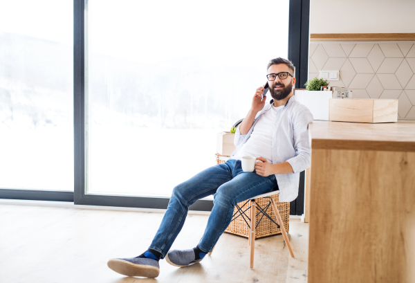 A mature man with coffee and smartphone moving in new home, making a phone call.